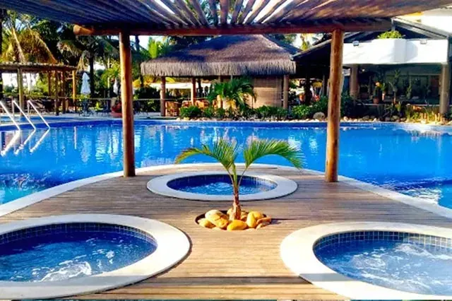 Piscina do resort com pergolado de madeira, ofurôs e cabana de palha