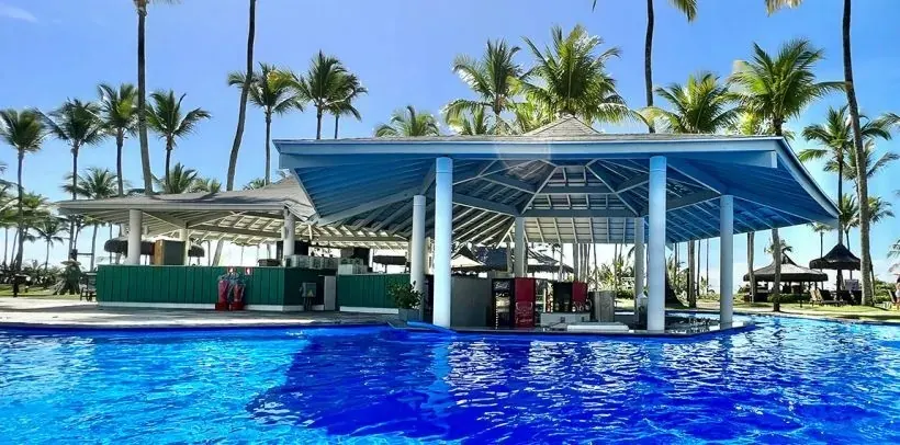 Piscina do resort com bar central de telhado azul entre coqueiros